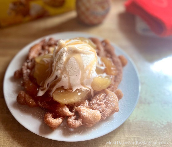 This indulgent Apple Pie funnel cake is a theme park-inspired treat that brings the magic home! Made with a quick Bisquick batter, it's fried to crispy perfection, sprinkled with powdered sugar, and loaded with dozy apple pie filling, creamy vanilla ice cream, and a caramel drizzle.