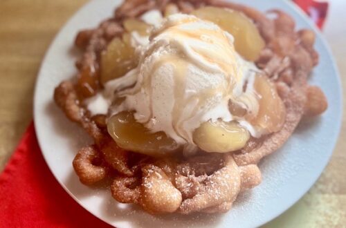 This indulgent Apple Pie funnel cake is a theme park-inspired treat that brings the magic home! Made with a quick Bisquick batter, it's fried to crispy perfection, sprinkled with powdered sugar, and loaded with dozy apple pie filling, creamy vanilla ice cream, and a caramel drizzle.