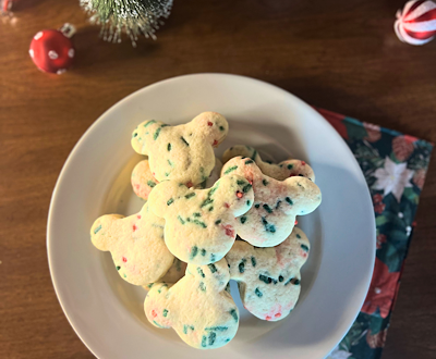 A plate of homemade Mickey-shaped Christmas Confetti Cookies with red & green sprinkles, set against a background of festive holiday decorations.
