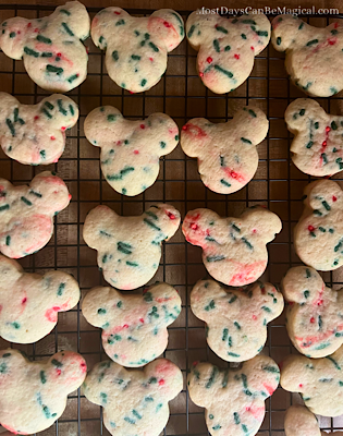 Rows of Mickey-shaped Christmas Confetti Cookies with festive red & green sprinkles cooling on a wire rack.