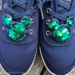 A pair of Mickey shoe clips decorated with blue and green sequins clip to a pair of navy lace-up shoes.