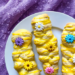 Three golden sweet braids drizzled with lemon glaze and decorated with colorful edible flowers on a white plate over a purple tablecloth.