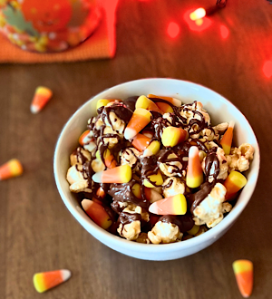 White bowl filled with caramel popcorn, chocolate drizzle, colorful candy corn, and a sprinkle of sea salt - a festive Disney-inspired Halloween movie night snack!