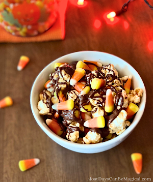 White bowl filled with caramel popcorn, chocolate drizzle, colorful candy corn, and a sprinkle of sea salt - a festive Disney-inspired Halloween movie night snack!