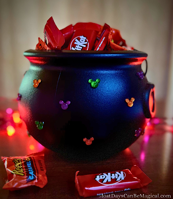 Disney-inspired black cauldron with Halloween-colored Mickey-shaped rhinestones hot glued to it is filled with candy. A magical DIY craft.