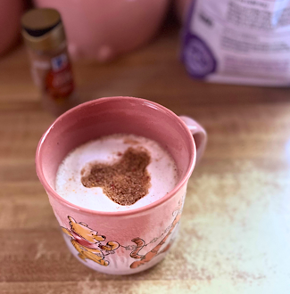 Chai latte in a pink Winnie the Pooh mug topped with a Mickey-shaped design in the foam.
