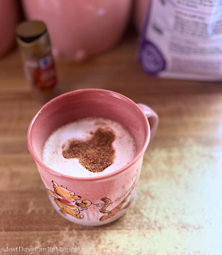 Chai latte in a pink Winnie the Pooh mug topped with a Mickey-shaped design in the foam.