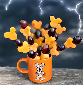Cup of Disney-inspired Halloween Fruit skewers featuring Mickey-shaped cantaloupe and grapes with a stormy sky background.