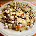 Disney-inspired Caramel apple nachos on a white plate topped with mini marshmallows, festive sprinkles, caramel, white chocolate, mini chocolate chips, and sea salt.