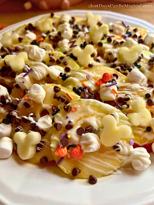 Disney-inspired Caramel apple nachos on a white plate topped with mini marshmallows, festive sprinkles, caramel, white chocolate, mini chocolate chips, and sea salt.