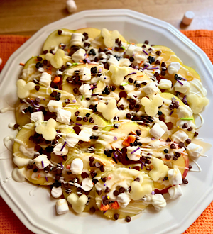 Overhead view of Disney-inspired Caramel apple nachos on a white plate topped with mini marshmallows, festive sprinkles, caramel, white chocolate, mini chocolate chips, and sea salt.