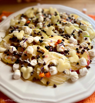Disney-inspired Caramel apple nachos on a white plate topped with mini marshmallows, festive sprinkles, caramel, white chocolate, mini chocolate chips, and sea salt.