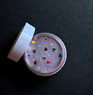 A small jar of Disney inspired homemade slime with glow in the dark make shaped glitter and multicolored Mickey shaped glitter sits with its lid off.