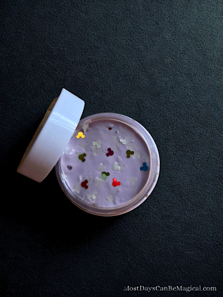A small jar of Disney inspired homemade slime with glow in the dark make shaped glitter and multicolored Mickey shaped glitter sits with its lid off.