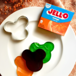 Plate with a box of orange gelatin mix, a Mickey-shaped cookie cutter and gelatin jigglers - a fun Disney-inspired Halloween finger food!