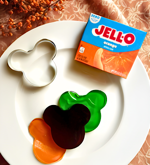 Plate with a box of orange gelatin mix, a Mickey-shaped cookie cutter and gelatin jigglers - a fun Disney-inspired Halloween finger food!