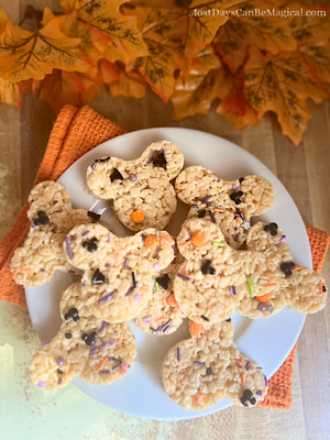 A plate of Disney-inspired Mickey-shaped Rice Krispies Treats with Halloween sprinkles and autumn leaves in the background.