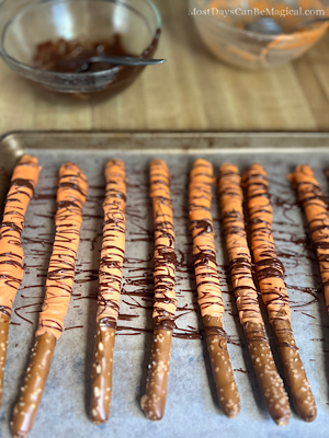 In the process of making Disney-inspired pretzel rods featuring a Tigger-Tail theme - the freshly dipped pretzels are drying on a baking sheet.