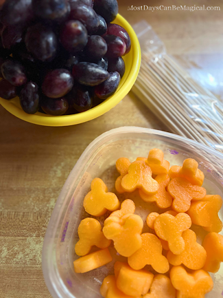 Purple grapes and Mickey-shaped cantaloupe along side bamboo skewers are waiting to be assembled.