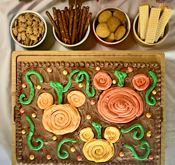 Buttercream board with Mickey-shaped pumpkins in different shades of orange in a chocolate buttercream pumpkin patch with assorted snacks for dipping.