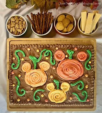 Buttercream board with Mickey-shaped pumpkins in different shades of orange in a chocolate buttercream pumpkin patch with assorted snacks for dipping.
