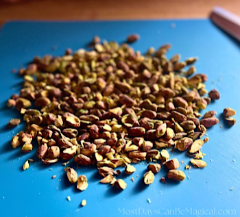 Roughly chopped pistachios on a blue cutting mat waiting to be put into cookie dough.
