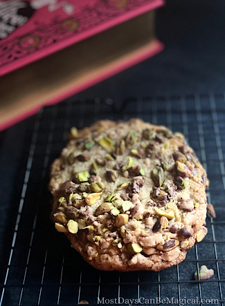 Colossal Pistachio Toffee Cookie on a cooling rack with a large pink book in the background and a few pistachios sprinkled around.