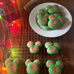 Disney-inspired Christmas cookies on a rack with a plate of them in the background and Christmas lights.