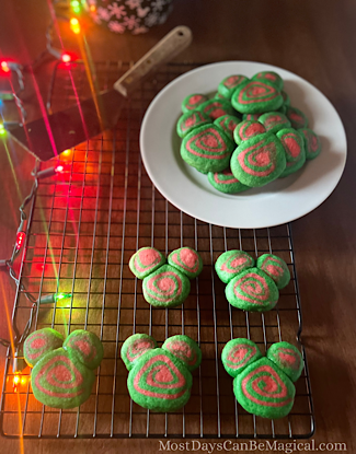 Disney-inspired Christmas cookies on a rack with a plate of them in the background and Christmas lights.