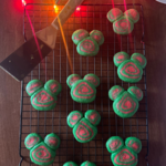 Disney-inspired Christmas cookies on a rack with a plate of them in the background and Christmas lights.