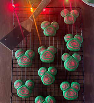 Disney-inspired Christmas cookies on a rack with a plate of them in the background and Christmas lights.