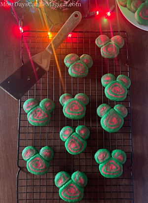 Disney-inspired Christmas cookies on a rack with a plate of them in the background and Christmas lights.