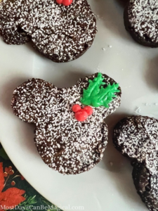 Up close shot of a Mickey-shaped brownie dusted with powdered sugar with Mickey-shaped holly berry and leaves piped out of icing.